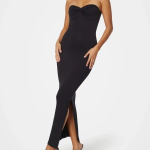 Svart axelbandslös långklänning med slits - Säljer en svart axelbandslös långklänning med twistad detalj vid bysten och slits framtill. Klänningen har en tight passform och är tillverkad i ett ribbat material som ger en snygg siluett. Perfekt för dig som vill ha en stilren och elegant look. Annonsen tas bort 31maj, helt ny med prislapp ❤️