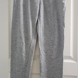 Grå mjukisbyxor från Champion - Säljer ett par grå mjukisbyxor från Champion i storlek X-Large för ungdom. Byxorna har en enkel design med Champion-logga på ena benet och är tillverkade i mjukt material som passar perfekt för chill eller träning.