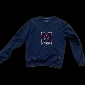 Mörkblå sweatshirt från Morris - Säljer en mörkblå sweatshirt från Morris med stort M och MORRIS-tryck på bröstet. Tröjan har rund halsringning och långa ärmar. Perfekt för en stilren och avslappnad look.