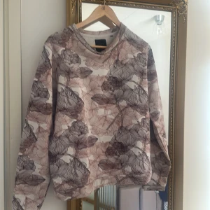 Blommig långärmad tröja från Saints and Mortals - Säljer en snygg långärmad tröja från Saints and Mortals i storlek medium. Tröjan har ett blommigt mönster i beige och bruna toner, perfekt för dig som gillar en unik och stilren look.