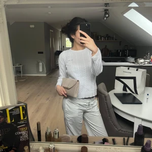 Vit kabelstickad tröja  - Säljer en vit kabelstickad tröja från Bondelid med rund halsringning och diskret broderad logga på bröstet. Tröjan har lång ärm och ribbade muddar vid ärmslut och nederkant. Perfekt för lager-på-lager och enkel att matcha.