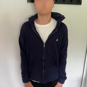 Mörkblå hoodie från Polo Ralph Lauren - Mörkblå hoodie från Polo Ralph Lauren. Ett litet hål vid armen men som man knappast ser!!😀 annars är den i väldigt fin skick. Hör av dig vid frågor.