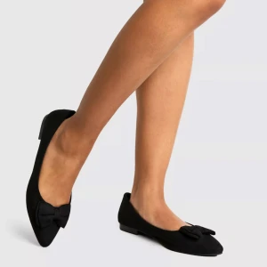 Ballerinaskor - Säljer ett par svarta ballerinaskor från Boohoo med spetsig tå och dekorativ rosett framtill. Skorna har en platt sula och är tillverkade i mockaliknande material. Perfekta för dig som vill ha en stilren och söt look.