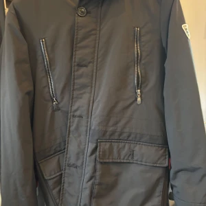 Svart jacka med teddyfoder från deval - Säljer en svart jacka från deval med mysigt beige teddyfoder. Jackan har två snedställda bröstfickor med dragkedja, stora fickor framtill och knappstängning. Perfekt för kyliga dagar och har en snygg patch på ärmen.