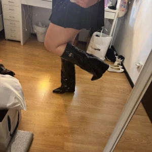 Folded boots - Säljer ett par svin snygga svarta boots i lack med spetsig tå och bälte upptill. Stövlarna har dragkedja på insidan och en hög klack. Perfekta för dig som vill sticka ut! Dessa har jag endast provat på. Säljer på grund av att jag har för stora lår så det sitter väldigt tajt på mig. Dessa boots är i storlek 38. 