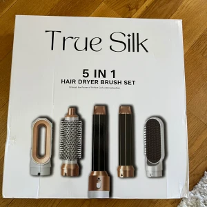 True Silk 5 in 1 hårstyler - True Silk 5 in 1 hårstyler med utbytbara borsthuvuden i vitt och roséguld. Setet innehåller olika borstar och locktillbehör för styling av håret, inklusive rundborste och fönmunstycke. Perfekt för att skapa volym, lockar och släta frisyrer.