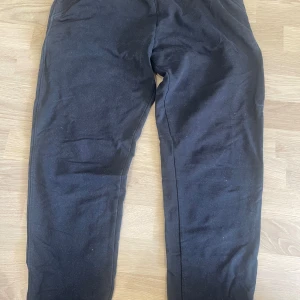 Svarta mjukisbyxor med resår och snörning - Svarta mjukisbyxor med resår i midjan och snörning. Byxorna har muddar vid bensluten och är tillverkade i mjukt bomullsmaterial. Perfekta för en avslappnad stil.