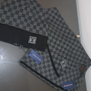 Grå och svart rutig halsduk  - Säljer en lyxig halsduki grått och svart med klassiskt rutigt mönster och logga. Halsduken har en mjuk och stilren design, perfekt för att lyfta din outfit. Kommer med originaltaggar.