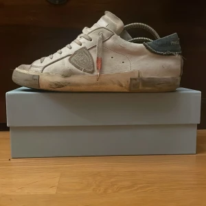 Vita Philippe Model sneakers med blå jeans detalj - Säljer ett par vita Philippe Model sneakers med blå jeans detalj på hälen och vit snörning. Skorna har en klassisk låg sneakersdesign med rund tå och platt sula. Märkeslogga syns på hälen och sidan. Perfekta för en stilren vardagslook. Storlek 43. Skorna är välanvända men inga större defekter utan bara naturlig slitning. Priset är inte hugget i sten och jag är villig att förhandla. Box medföljer!