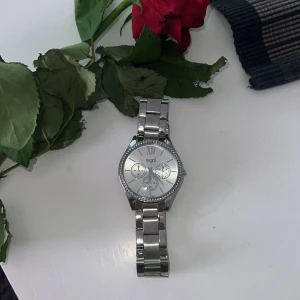  Klocka från Regal - Stilren klocka från Regal i silverfärgat metallarmband och boett. Urtavlan är också silver med tre mindre urtavlor och romerska siffror vid tolvslaget. Runt boetten sitter små glittrande stenar för extra detalj♥️