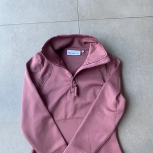 Rosa Ridtröja  från PS of Sweden - Säljer en snygg rosa långärmad träningströja från PS of Sweden i storlek XS. Men passar S. Tröjan har halv dragkedja framtill, meshdetaljer på axlarna och figurnära passform. Perfekt för ridning eller träning.