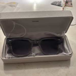 Gråtonade solglasögon från CHIMI - Snygga solglasögon från CHIMI med transparent grå båge och mörka glas. Modellen har en fyrkantig form och levereras i originalfodral med putsduk. Perfekt accessoar för att lyfta din stil. Säljer då dem inte kommer till användning. Pris kan diskuteras 