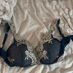 Mörkblå spets-bh med broderade detaljer - Säljer en mörkblå bh med vackra ljusa spetsdetaljer och broderade blommor. Bh:n har justerbara axelband och bygel för extra stöd. Perfekt för dig som vill ha något både snyggt och bekvämt under kläderna.