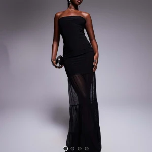 Svart axelbandslös långklänning - Helt ny klänning från ASOS.  svart axelbandslös långklänning med tight passform och transparent nederdel. Klänningen har en elegant och stilren design, perfekt för dig som vill sticka ut på festen. Materialet är mjukt och följsamt.