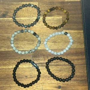 Set med sex pärlarmband i olika färger - Säljer ett set med sex elastiska armband med runda pärlor i olika färger och stenmönster. Färgerna är svart, grå, brun, vit och blå. Perfekt att mixa och matcha för en personlig stil.