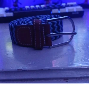 Blått och svart flätat bälte med läderdetaljer - Säljer ett snyggt flätat bälte i blått och svart med bruna läderdetaljer och silverspänne. Perfekt accessoar för att lyfta din outfit. Bältet har ett klassiskt spänne och är flexibelt i storleken. De är ljus blå och mörkblå den är ca typ 80 cm lång och är utsträckt bar är prutbar vid snabbaffär skriv om du har några frågor eller funderingar 