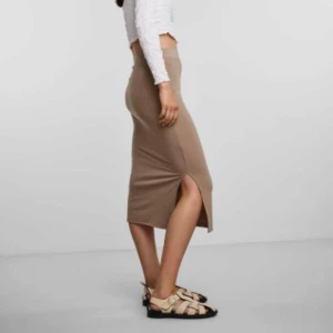 Beige ribbad kjol med slits från PIECES - Säljer en beige ribbad kjol från PIECES i midilängd. Kjolen har en snygg slits på sidan och resår i midjan för extra komfort. Perfekt att styla med en croppad topp eller stickad tröja.
