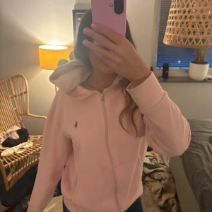 Rosa hoodie från Ralph Lauren - Säljer en snygg rosa hoodie från Ralph Lauren med dragkedja och en blå logga på bröstet. Perfekt för en avslappnad stil. Hör av dig vid intresse! 💖
