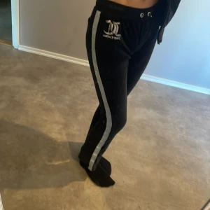 Ett svart sätt från Juicy Couture  med silverdetaljer - Säljer ett par svarta mjukisbyxor och en tröja från Juicy Couture med breda silverfärgade ränder längs sidorna och logga framtill. Byxorna har dragsko i midjan och är perfekta för en avslappnad stil. Tröjan har juice couture signatur på baksidan. Köptes två år sedan.