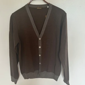 Stenströms kofta - Säljer en brun kofta från Stenströms i 100% merino extrafine. Koftan har gråa detaljer längs knäppningen, ärmslut och nederkant samt knappar framtill. Perfekt för dig som gillar klassisk och stilren design. Nypris: 2300