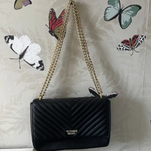 Svart quiltad axelväska från Victoria's Secret - Säljer en svart quiltad axelväska från Victoria's Secret med guldfärgad kedja. Mycket bra skick förutom runt magnetknappen. Runt mycket i den 