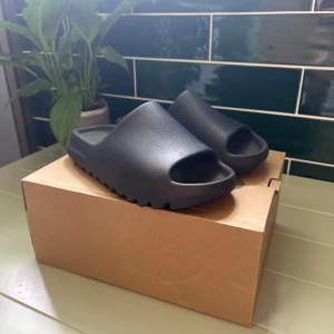 Yeezy Slides onyx - Säljer ett par svarta Yeezy Slide från Adidas i storlek 42. De har en chunky, modern design med öppen tå och räfflad sula. Tillverkade i syntetmaterial för en clean och minimalistisk look. Perfekta för chill dagar eller när du vill ha något bekvämt och stilrent på fötterna. Knappt använda max 5 gånger. Tveka inte på att ställa frågor!!!