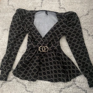 Svart mönstrad blus från Amisu!! - Supersnygg svart blus från Amisu med beige kedjeinspirerat mönster, markerade axlar och lång ärm. Djup v-ringning och bälte med guldfärgat spänne i midjan ger en riktigt trendig siluett. Perfekt för dig som gillar statement-plagg! Är i storlek XS är också lite större än på bilden💕