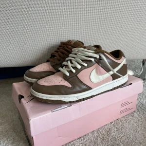 Nike SB Dunk Low ’Stüssy cherry’ - Nike SB Dunk Low Stüssy cherrys med original box och väldigt bra skick. Ända defekten är ett väldigt litet hål i baksidan av vänstra skon. Både rosa och bruna snören. Har inget kvitto därav priset.