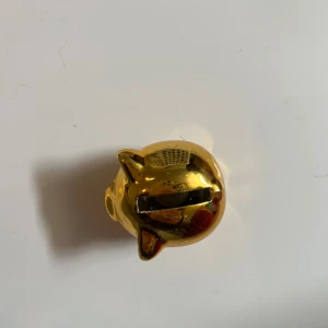 Guldig spargris i keramik - Söt spargris i glänsande guld med klassisk rund form och fyra små ben. Perfekt som dekoration eller för att spara mynt. Grisen har ett myntinkast på ryggen och öppning undertill med plastlock. Ger ett lyxigt intryck med sin spegelblanka yta. Helt ny. Liten och gullig!