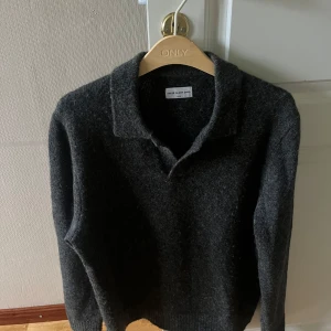 Mörkgrå stickad tröja med krage - Snygg mörkgrå stickad tröja från These Glory Days med klassisk krage och lång ärm. Perfekt för dig som gillar en stilren och enkel look. Mjuk och skön, passar till många outfits.