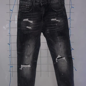 Svarta slitna skinny jeans - Säljer ett par svarta skinny jeans med slitningar och hål på knäna. Jeansen har en tvättad look med vita färgstänk och klassiska fem fickor. Perfekta för en edgy streetstyle.