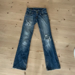 Lågmidjade blå bootcut jeans från Lee med slitningar - Säljer mina gamla favorit jeans tyvärr, jag har tyvärr växt ur dom. Tredje bilden är lånad av tjejen jag köpte jeansen av förut, jag tycker dom sitter lite lägre och på ett annat sätt på mig en vad dom sitter på henne men de e ju från person till person. Dom är ett par blå bootcut jeans från Lee med slitningar och hål på benen samt lite slitna längst ner där bak. Midjemåttet är ca 74 runt om och 76 i innerbenslängt