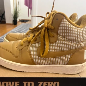 Bruna Nike sneakers med rutigt mönster - Säljer ett par unika bruna Nike sneakers med rutigt mönster i vitt och brunt på sidorna. Skorna har snörning, vit sula och mjuk fuskpäls på insidan för extra komfort. Perfekta för dig som vill sticka ut med din stil.