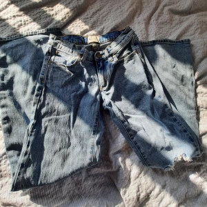 Blåa wide jeans  - Säljer ett par ljusblå jeans med breda ben och ett stort hål på ena knät. Klassisk femficksmodell med raka sömmar och vintagekänsla. Perfekta för dig som gillar en avslappnad och trendig look. SÄLJER FLER JEANS!!!❤️❤️❤️