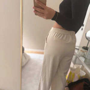Beiga vida byxor med resårmidja - Säljer ett par beiga byxor med breda ben och resår i midjan. Byxorna har en avslappnad passform och är perfekta för en stilren och bekväm look. Passar bra till både crop tops och stickade tröjor.