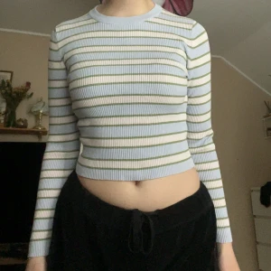 Randig croppad tröja från Zara - Säljer en croppad långärmad tröja från Zara i ljusblått, vitt och olivgrönt. Tröjan är ribbad och har ett smalt randigt mönster. Perfekt för dig som gillar en enkel men snygg stil. Rund halsringning och mjukt material. Står L, men är mer av en tight fit, så S eller M. 