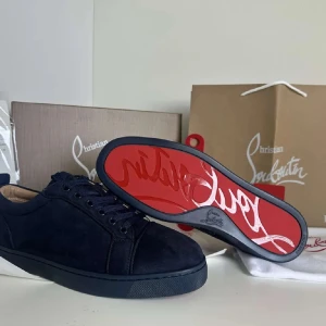 Christian Louboutin Skor - Säljer ett par svarta sneakers från Christian Louboutin i mocka med den ikoniska röda sulan. Skorna har rund tå, platt sula och diskret broderad logga på hälen. Perfekta för dig som gillar stilrena och exklusiva sneakers.