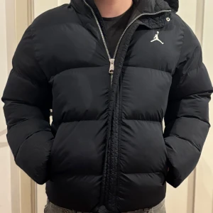 Svart pufferjacka från Jordan - Säljer en svart pufferjacka från Jordan med huva och dragkedja framtill. Jackan har en klassisk pufferdesign med diskret logga på bröstet och två sidofickor. Perfekt för kyliga dagar och riktigt skön att bära. Varan är köpt för 3,500, och har använts i 2 vintrar o sitter bra . Den är även väldigt varm ! 