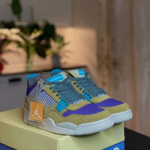 Nike Air Jordan 4 Union LA Desert Moss - Nike Air Jordan 4 Union LA Desert Moss med lila mesh, olivgröna mockadetaljer och blåa accenter. Skorna har vit sula med gula och blå detaljer undertill, samt klassisk snörning och meshpaneler på sidorna. Perfekt för dig som vill sticka ut med färg och stil.