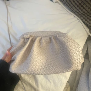 Beige kuvertväska i ormskinnsmönster - Säljer en beige kuvertväska med snyggt ormskinnsmönster och mjuk struktur. Väskan har en rymlig öppning med metallstängning och är perfekt för att bära det viktigaste. Tillverkad i syntetmaterial med lyxig känsla och stilren look.