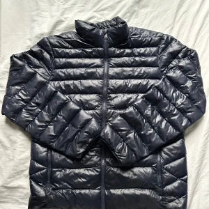 Dunjacka från Polo Ralph Lauren - Snygg tunnare mörkblå dunjacka från Polo Ralph Lauren med broderad logga på bröstet. Jackan har quiltad design, hög krage och dragkedja framtill. Perfekt till hösten och våren men även vintern. Nypris ca 3500kr. Pris ej hugget i sten!