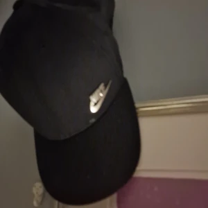 Svart keps från Nike - Snygg svart keps från Nike med klassisk böjd skärm och silverfärgad Nike-logga framtill. Perfekt accessoar för en sportig och stilren look. Justerbar passform baktill.