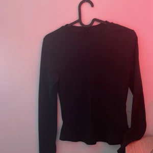 Svart långärmad tröja i bomull - Enkel svart långärmad tröja med rund hals. Tröjan har en klassisk passform och är tillverkad i mjukt bomullsmaterial, perfekt att styla med jeans eller kjol. Snygg och basic för en clean look.