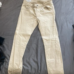 Beiga jeans från J.Lindeberg - Snygga beiga jeans från J.Lindeberg med klassisk femficksdesign och diskret logga på bakre läderpatchen. Byxorna har normal passform och är perfekta för en stilren look. Tillverkade i mjuk bomull för extra komfort.