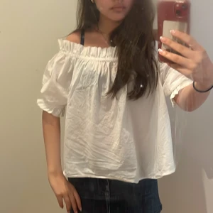 Vit offshoulder blus - Säljer en luftig vit offshoulder blus med resår vid axlarna och korta puffärmar. Perfekt för varma dagar och enkel att styla med jeans eller kjol. Blusen har en avslappnad passform och är gjord i ett mjukt bomullstyg.