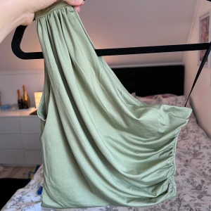 Grön oneshoulder topp (NY) - Snygg grön oneshoulder topp från H&M i ett mjukt och följsamt material. Toppen har en draperad design och har dubbelt tyg. Perfekt för en stilren look 💚 Använd 1 gång. Önskar du veta exakta mått? Tveka inte att höra av dig!