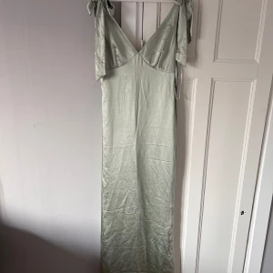Ljusgrön långklänning från Pretty Lavish - Elegant ljusgrön långklänning från Pretty Lavish i ett mjukt och glansigt material. Klänningen har en v-ringad design med knytband vid axlarna för en extra touch. Perfekt till balen💚använd en gång!