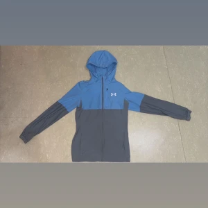 Under armour jacka  - Säljer en blå och grå jacka från Under Armour. Jackan har en huva och dragkedja framtill. Perfekt för träning storlek XS