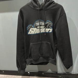 Svart hoodie från Trapstar - Snygg svart hoodie från Trapstar med ett stort tryck på framsidan som säger 'London Shooters'. Den har en klassisk känguruficka och justerbar huva med dragsko. Perfekt för en casual look.