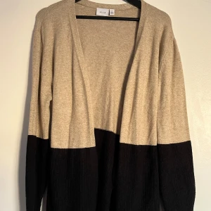 Beige och svart kofta från Vila - Säljer en snygg beige och svart kofta från Vila. Koftan har långa ärmar och ett knytband i ryggen för en fin passform. 